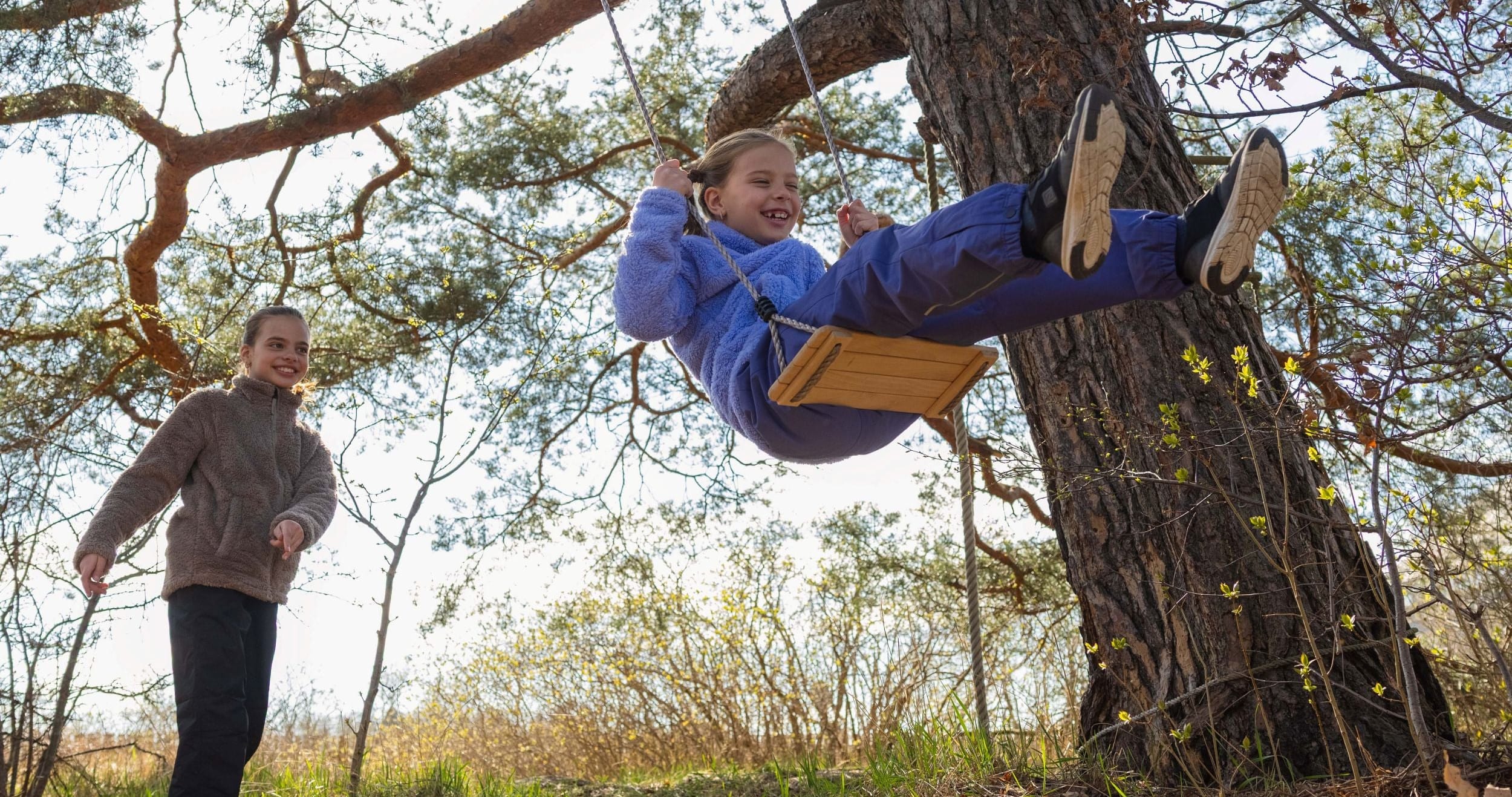 Person swinging on a swing set in a tree with another person standing below.
