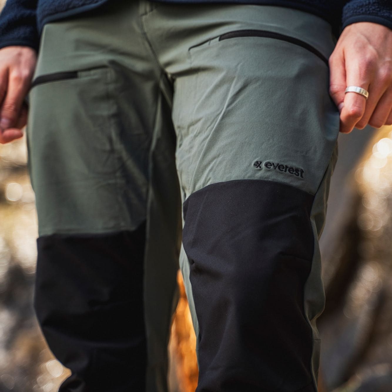 Person wearing green and black pants with a brand logo, standing outdoors.