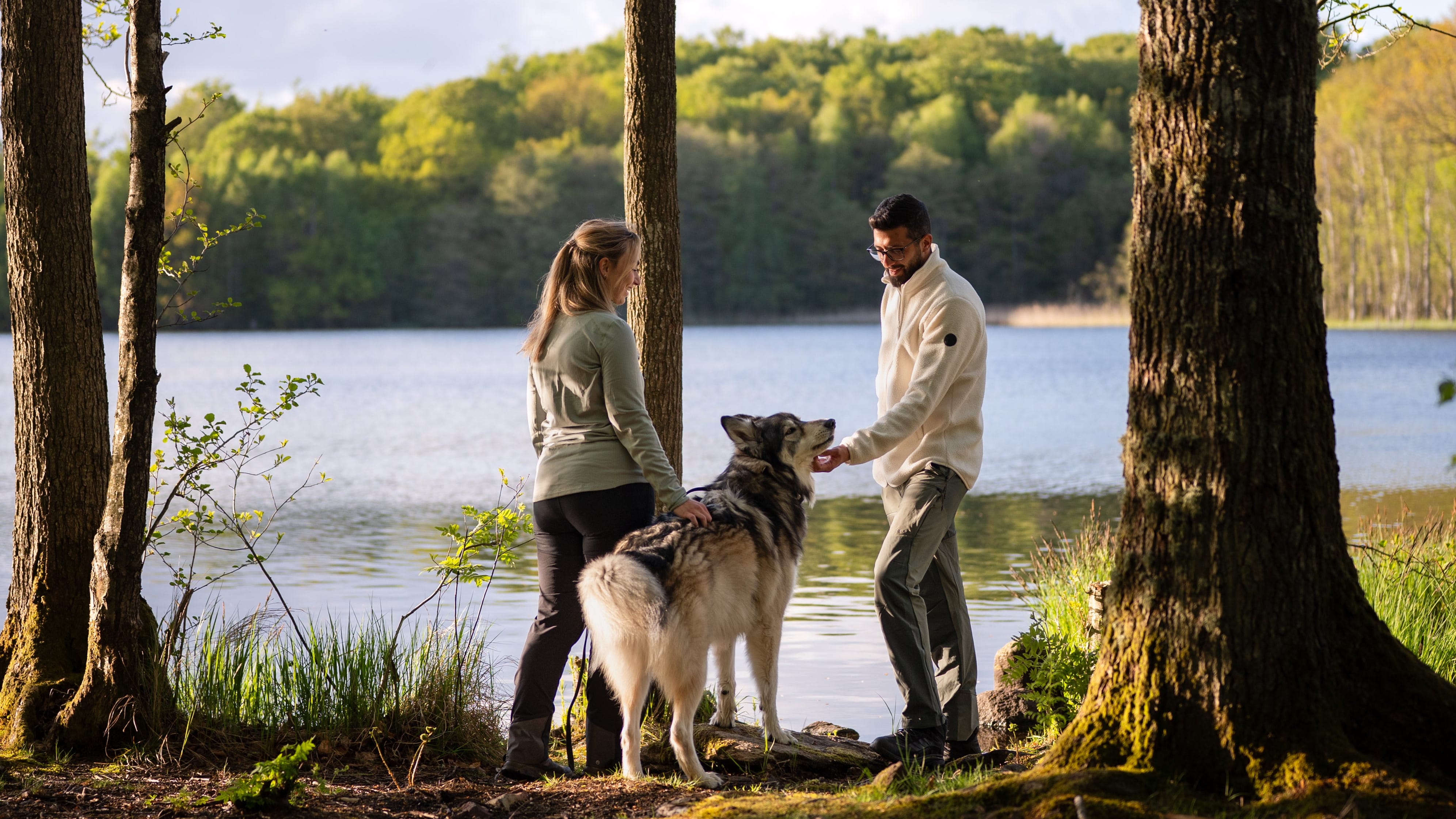 Two people with a dog by a lake in a forest