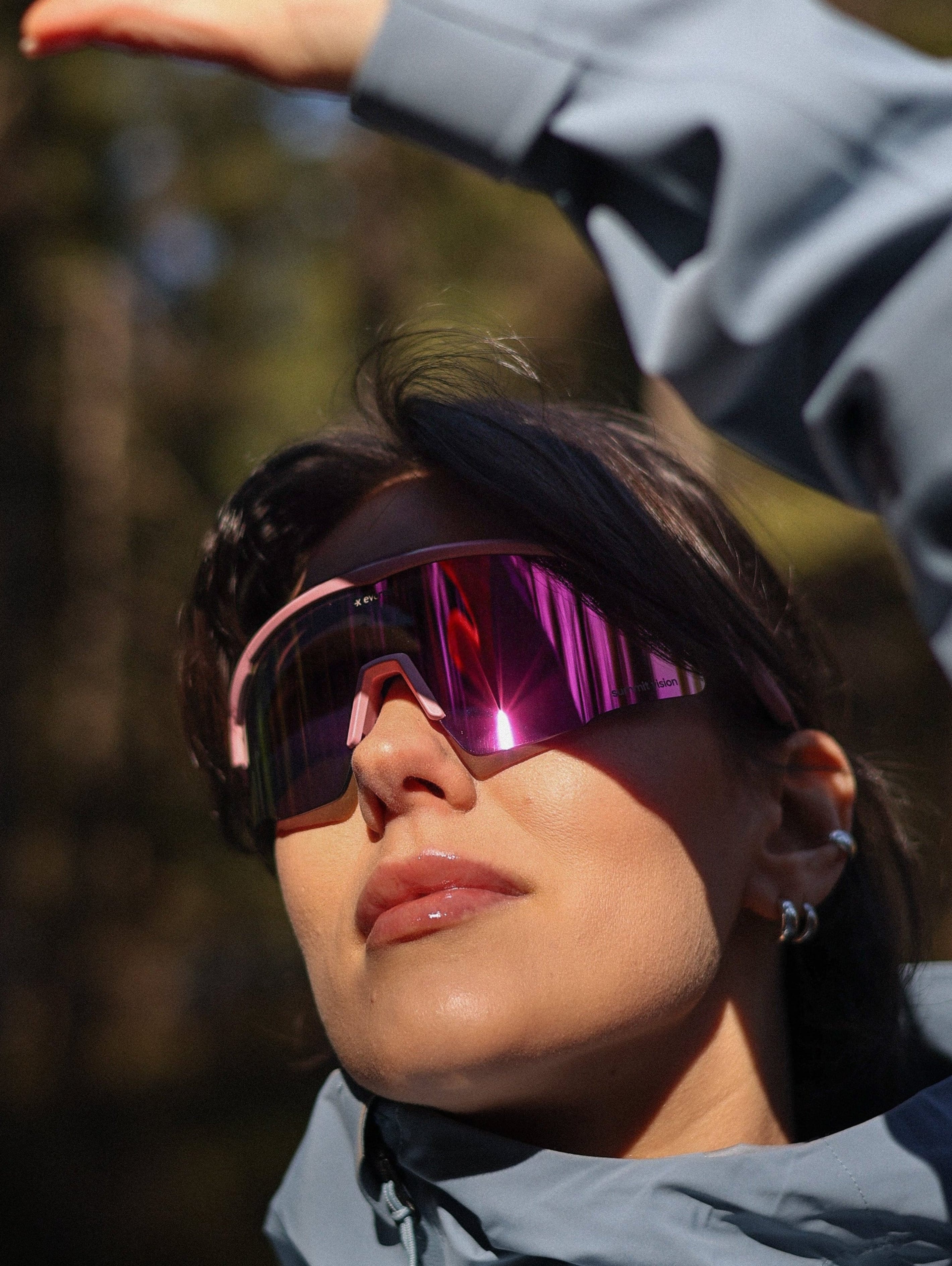 Person wearing a gray jacket and pink-tinted sunglasses with a blurred natural background